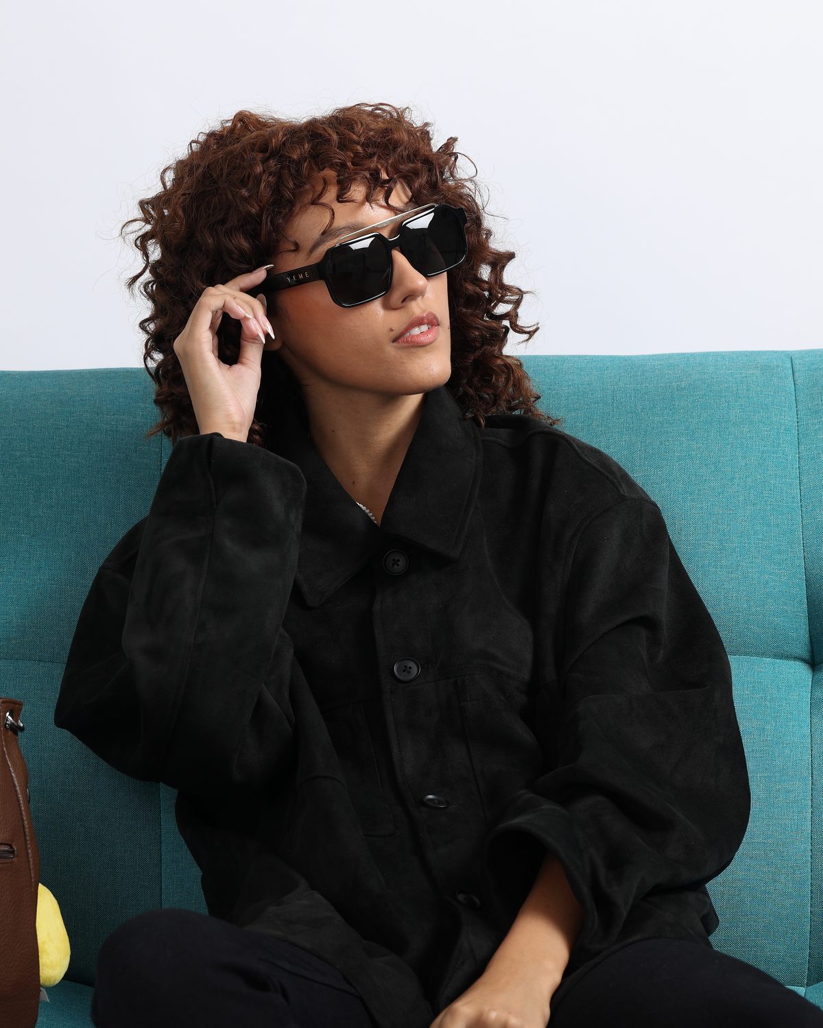 Woman on a teal sofa wearing YEME Ice sunglasses with black lenses