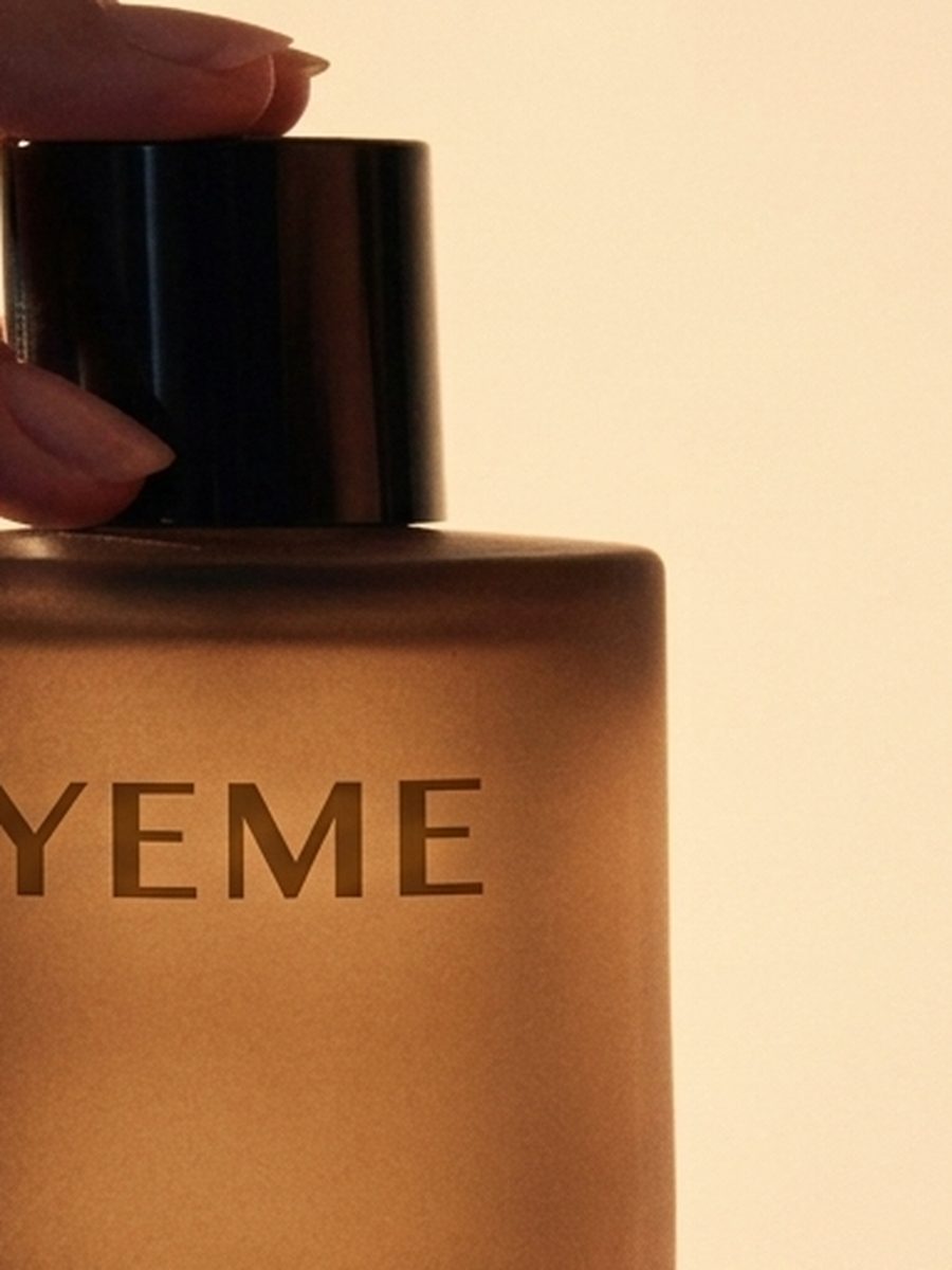 Hand lifting the black cap of a YEME fragrance bottle